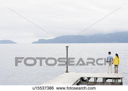Young couple standing on jetty and looking at view View Large Photo Image Stock Photograph - Young couple standing on jetty and looking at view. Fotosearch
