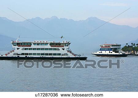 Stock Photograph - 2 Passenger ferry boats in motion across Lake Como, Italy, in morning sunlight, with blue water, mountain range, and sky. Fotosearch