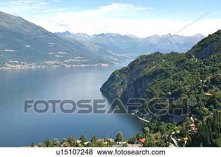 Aerial view of Lake Como with village in foreground and ring of hills and mountain range around calm blue water in morning sunlight View Large Photo Image Stock Photo - Aerial view of Lake Como with village in foreground and ring of hills and mountain range around calm blue water in morning sunlight. Fotosearch