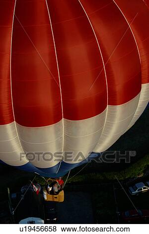 Stock Photo - Aerial view of red white and blue striped hot air balloon over ground at night, with cars below in shadows . Fotosearch