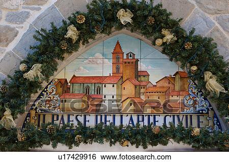 Stock Photograph - Antique ceramic wall plaque, Deruta, celebrating tradition of majolica ware production, surrounded by Christmas decorations, illuminated for festive season. Fotosearch