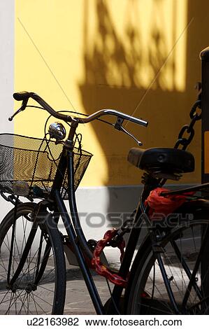 Stock Image - Black bicycle parked against black chain with yellow wall background, in late afternoon sun, Florence, Italy. Fotosearch