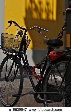 Stock Photo - Black bicycle parked against black chain with yellow wall background, in late afternoon sun, Florence, Italy. Fotosearch