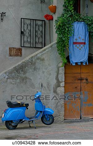Stock Photo - Blue motorbike parked outside wooden door with flag draped over entrance, as seen from public street. Fotosearch