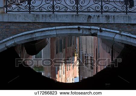 Stock Image - boats and building reflections on canal, under stone footbridge. Fotosearch