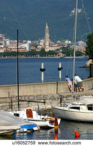 Stock Photo - Boats in harbour, with town, church spire, tourists, mountains in background, Lake Como, Italy,. Fotosearch