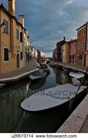 Picture - Boats moored along Burano canal, in sunlight before an evening summer storm. Fotosearch