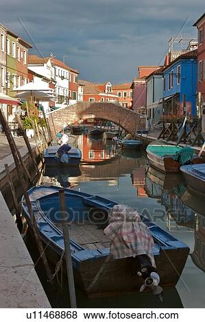 Stock Photo - Boats moored along Burano canal, in sunlight before an evening summer storm. Fotosearch