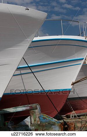 Stock Photograph - Bow detail, Scario harbour with boats in drydock against blue sky background with puffy clouds. Fotosearch