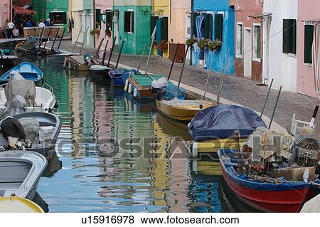 Stock Photo - Burano canal with moored boats and reflections of brightly coloured buildings. Fotosearch