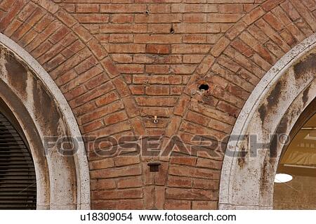 Picture - Close up of red brick arched column between 2 windows of Palazzo, showing detailed stonework and white stone arch on either side. Fotosearch