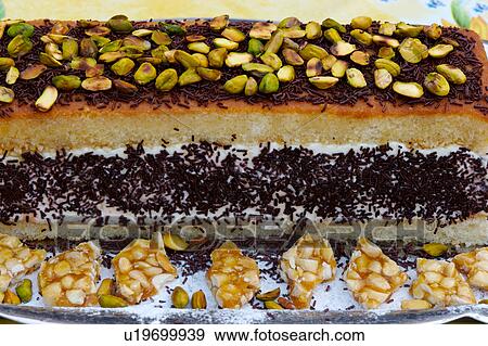 Stock Photo - Closeup of layered sponge cake, with cream and chocolate sprinkles, topped with pistachio nuts, and surrounded by nut brittle. Fotosearch