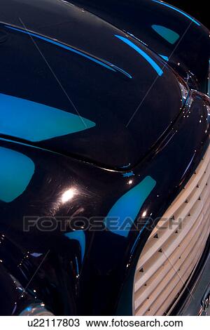 Stock Image - Detail of antique blue Ferrari, side front view, showing front grille and hood, under blue lighting. Fotosearch