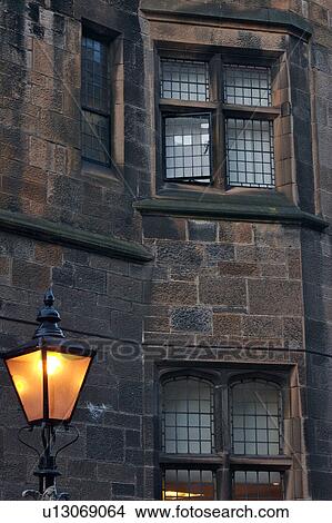 Picture - Detail of Glasgow University building, sandstone block with lead glass windows, and old iron lamp lit at dusk, Glasgow, Scotland. Fotosearch