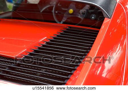 Stock Photograph - Detail of parked red Ferrari, rear view of back deck, rear window and steering wheel, on cloudy rainy day. Fotosearch