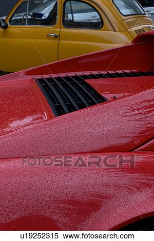 Stock Photography - Detail of parked red Ferrari, with yellow Fiat cinquecento, on cloudy rainy day. Fotosearch