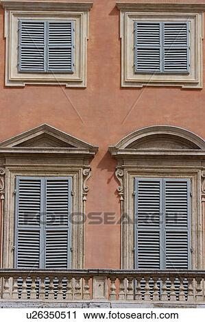 Stock Image - Detail of Renaissance palace, 4 windows with ornate stonework surround, orange/pink stucco exterior, stone balustrade. Fotosearch