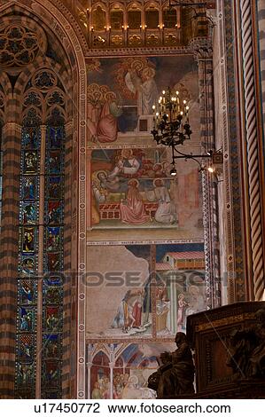 Stock Image - Detail of side of apse showing wall completely painted with frescoes, illuminated balcony, ornamental wrought iron lamps, and central stained glass window, with carved wooden pulpit in foreground. Fotosearch