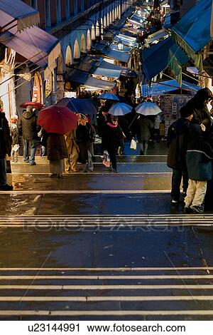 Stock Image - Evening shoppers in the rain with umbrellas from the Rialto Bridge, with open air market in background. Fotosearch