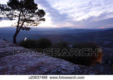 Evergreen tree silhouetted beside old stone town wall before sunrise, with view over Tiber valley in misty dawn of winter, river winding through valley, light dusting of snow and lights in valley View Large Photo Image Stock Photograph - Evergreen tree silhouetted beside old stone town wall before sunrise, with view over Tiber valley in misty dawn of winter, river winding through valley, light dusting of snow and lights in valley. Fotosearch