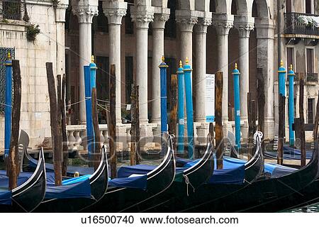Gondolas moored at canal side in winter rain with blue covers, columned arcade in background and blue mooring posts View Large Photo Image Stock Image - Gondolas moored at canal side in winter rain with blue covers, columned arcade in background and blue mooring posts. Fotosearch