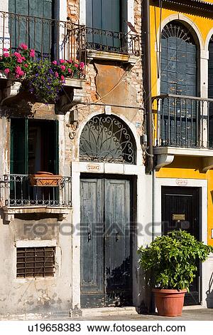 Stock Image - House facade, with wrought iron balconies around doors and windows, peeling paint, bright yellow walls, and pink flowers. Fotosearch