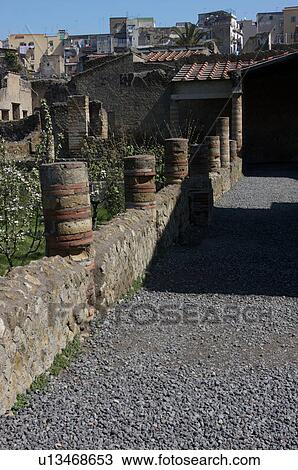 Stock Image - In the shadow of Vesuvius, the ruins of Ercolano - the Inn house, with modern town behind. Fotosearch