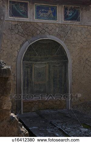 Stock Image - In the shadow of Vesuvius, the ruins of Ercolano - house detail of mosaic covered lararium. Fotosearch