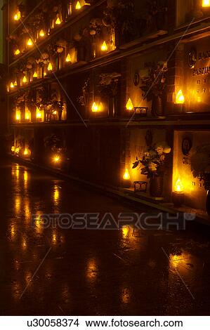 Picture - Italian cemetery with rows of flowers at tombs, night view in fog, with lights lit and reflected in wet paving. Fotosearch
