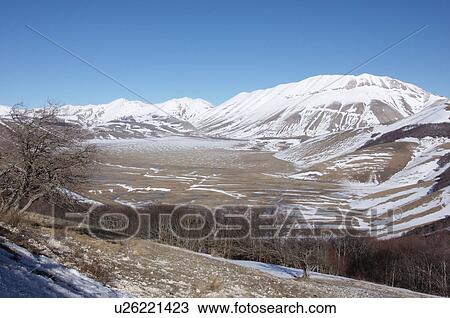 Landscape view of Piano Grande meadow, Umbria, with snow on mountains, brilliant sunshine and blue sky on cloudless winter day View Large Photo Image Stock Image - Landscape view of Piano Grande meadow, Umbria, with snow on mountains, brilliant sunshine and blue sky on cloudless winter day. Fotosearch