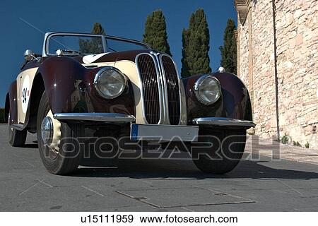 Low front-side view of black and white antique BMW, showing head lamps, grille and wheels, on road in Assisi, at Mille Miglia, with blue sky and cypress trees in background View Large Photo Image Stock Photo - Low front-side view of black and white antique BMW, showing head lamps, grille and wheels, on road in Assisi, at Mille Miglia, with blue sky and cypress trees in background. Fotosearch
