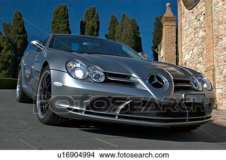 Low front-side view of silver Maclaren Mercedes car on road in Assisi, at Mille Miglia, with blue sky and cypress trees in background View Large Photo Image Picture - Low front-side view of silver Maclaren Mercedes car on road in Assisi, at Mille Miglia, with blue sky and cypress trees in background. Fotosearch