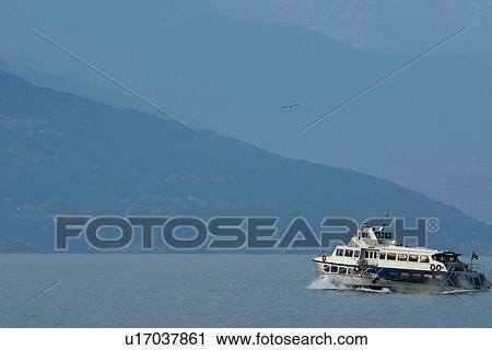 Passenger ferry boat in motion across Lake Como, Italy, in morning sunlight, with blue water, mountains, and sky View Large Photo Image Stock Image - Passenger ferry boat in motion across Lake Como, Italy, in morning sunlight, with blue water, mountains, and sky. Fotosearch