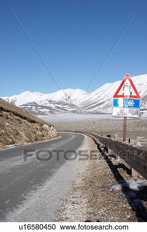 Road curving, and road sign at Piano Grande, Umbria, with snow on mountains, brilliant sunshine and blue sky on cloudless winter day View Large Photo Image Stock Image - Road curving, and road sign at Piano Grande, Umbria, with snow on mountains, brilliant sunshine and blue sky on cloudless winter day. Fotosearch