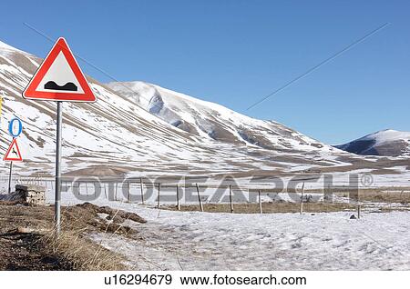 Roadside signage warning of uneven road, animals crossing and need for snow chains in Piano Grande, with fenced fields and mountain background on snowy winter day, with bright sunshine View Large Photo Image Stock Photo - Roadside signage warning of uneven road, animals crossing and need for snow chains in Piano Grande, with fenced fields and mountain background on snowy winter day, with bright sunshine. Fotosearch