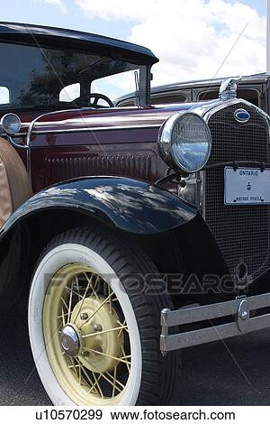 Stock Photo - Side front detail of old burgandy/blue Ford, showing front right wheel, with white yellow trim, headlamp, windscreen and hood, with blue sky background. Fotosearch