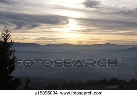 Sunrise over Tiber valley with grey pink and golden sky in the early morning mist of winter, with tree outline in foreground, View Large Photo Image Picture - Sunrise over Tiber valley with grey pink and golden sky in the early morning mist of winter, with tree outline in foreground,. Fotosearch
