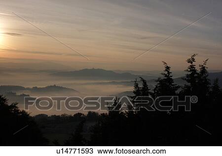 Sunrise over Tiber valley with grey pink and golden sky in the early morning mist of winter, with tree outline in foreground, and hilltop town of Todi in distance View Large Photo Image Stock Image - Sunrise over Tiber valley with grey pink and golden sky in the early morning mist of winter, with tree outline in foreground, and hilltop town of Todi in distance. Fotosearch
