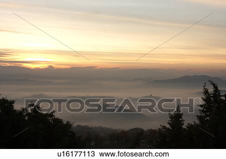 Sunrise over Tiber valley with grey pink and golden sky in the early morning mist of winter, with tree outline in foreground, and hilltop town of Todi in distance View Large Photo Image Stock Image - Sunrise over Tiber valley with grey pink and golden sky in the early morning mist of winter, with tree outline in foreground, and hilltop town of Todi in distance. Fotosearch