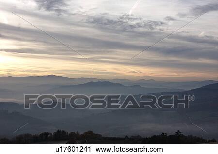 Sunrise over Tiber valley with grey pink and golden sky in the early morning mist of winter, with tree outline in foreground, and hilltop town of Todi in distance View Large Photo Image Stock Image - Sunrise over Tiber valley with grey pink and golden sky in the early morning mist of winter, with tree outline in foreground, and hilltop town of Todi in distance. Fotosearch