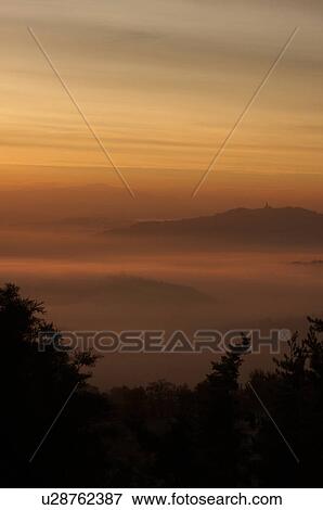 Sunrise over Tiber valley with grey pink and golden sky in the early morning mist of winter, with tree outline in foreground, and hilltop town of Todi in distance View Large Photo Image Stock Photo - Sunrise over Tiber valley with grey pink and golden sky in the early morning mist of winter, with tree outline in foreground, and hilltop town of Todi in distance. Fotosearch