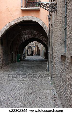 Stock Photography - View of 14th century street in Ferrara with Gothic arches and cobblestone paving, orange painted and brick houses. Fotosearch