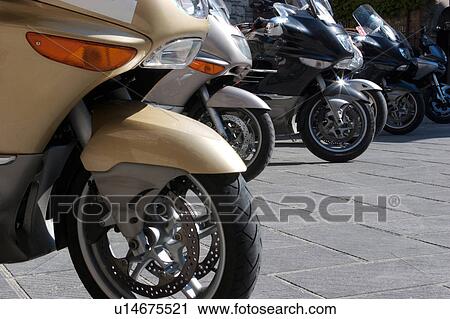 Stock Image - view of 6 motorbikes parked in a row, with front wheel cowling detail, on stone paving street, Umbria, Italy. Fotosearch