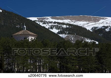Stock Photograph - View of abbey with evergreen trees and snow in mounains of Le Marche Italy. Fotosearch
