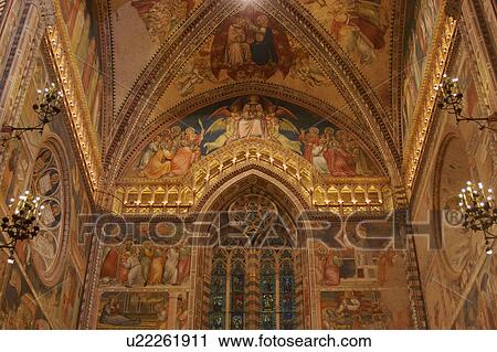 Stock Image - view of barrel vaulted ceiling, back and both side walls of apse, frescoes showing coronation of the Virgin, with trefoil stained glass window, illuminated balcony, and ornate wrought iron lamps. Fotosearch