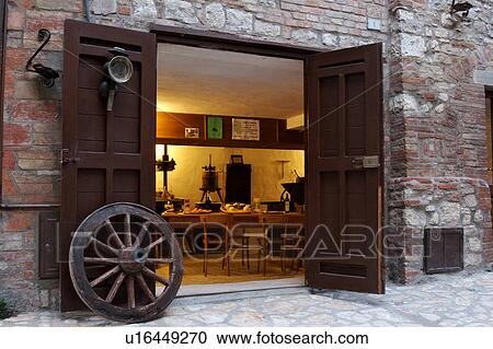 Stock Image - View of cantina from street, in historic centre of medieval village, showing table laid with local produce, cheese and hams, antique farming implements, and wagon wheel at entrance. Fotosearch
