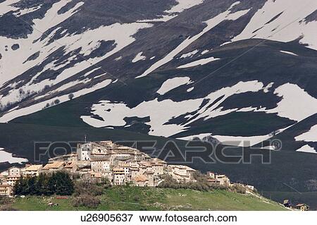 Stock Photo - View of Castellucio, Piano Grande, as the snows melt on the mountains behind the town, forming abstract patterns as a background to the dwarfed town. Fotosearch