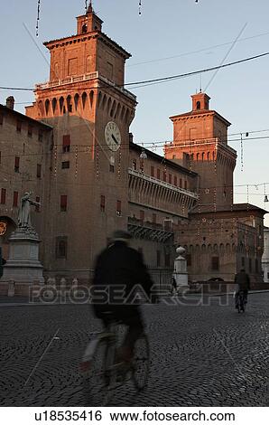 View of cobblestoned main street in front of Castello Estense, with statue of Savonarola, clock tower and Lion tower, and cyclists in road, Christmas illuminations at dusk View Large Photo Image Stock Photograph - View of cobblestoned main street in front of Castello Estense, with statue of Savonarola, clock tower and Lion tower, and cyclists in road, Christmas illuminations at dusk. Fotosearch