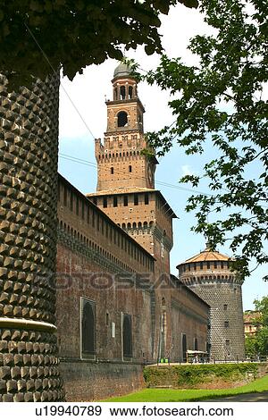 Stock Photo - View of exterior walls and fortifications of Castello Sforzesca, Milan, with round bastions, central Clock tower framed by trees and blue summer sky. Fotosearch