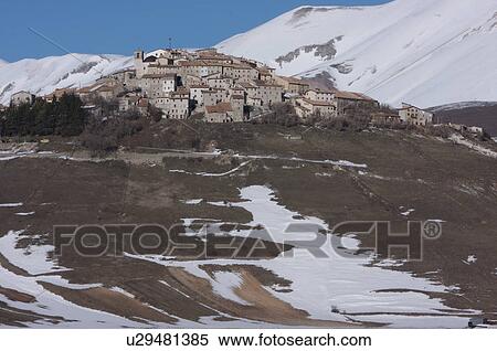 Stock Photography - View of hilltop village of Castellucio Piano Grande, Umbria, with snow on mountains, brilliant sunshine and blue sky on cloudless winter day. Fotosearch
